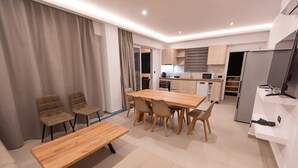 A modern kitchen with a dining area, including a wooden table and chairs, a sofa, and a TV. - Sinani Villas Rhodes - Private Pool Getaway (Rhodes)