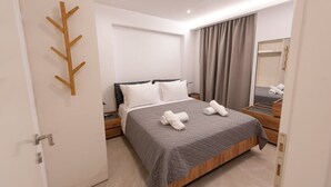 A modern hotel room with a large bed, a wooden headboard, a bedside table with a lamp, a mirror, and a door with a wooden coat rack. - Sinani Villas Rhodes - Private Pool Getaway (Rhodes)