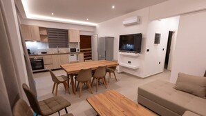 A modern living room with a wooden dining table, beige sofa, and a TV mounted on the wall. - Sinani Villas Rhodes - Private Pool Getaway (Rhodes)