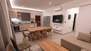Un salon moderne avec une table à manger en bois, un canapé beige et un téléviseur fixé au mur.