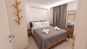 Une chambre d’hôtel moderne avec un grand lit, une tête de lit en bois, une table de chevet avec une lampe, un miroir et une porte dotée d’un porte-manteau en bois.