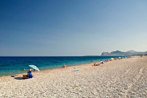 A pebbled beach with people sunbathing and swimming, a clear blue sky, and distant mountains. - Sinani Villas Rhodes - Serene Cozy Getaway (Rhodes)