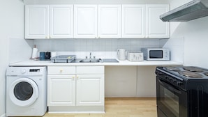 Een compacte keuken met witte kastjes, een wasmachine, een magnetron, een broodrooster en een fornuis.