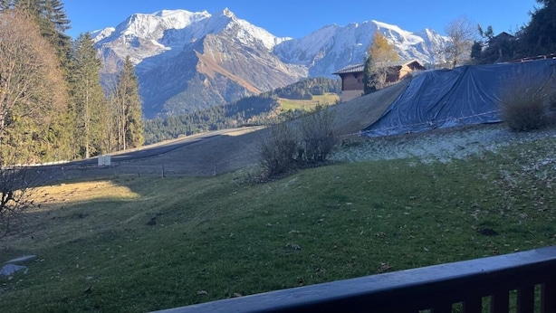 Paisaje montañoso con cielo despejado, zona cubierta de hierba y un edificio de techo inclinado.