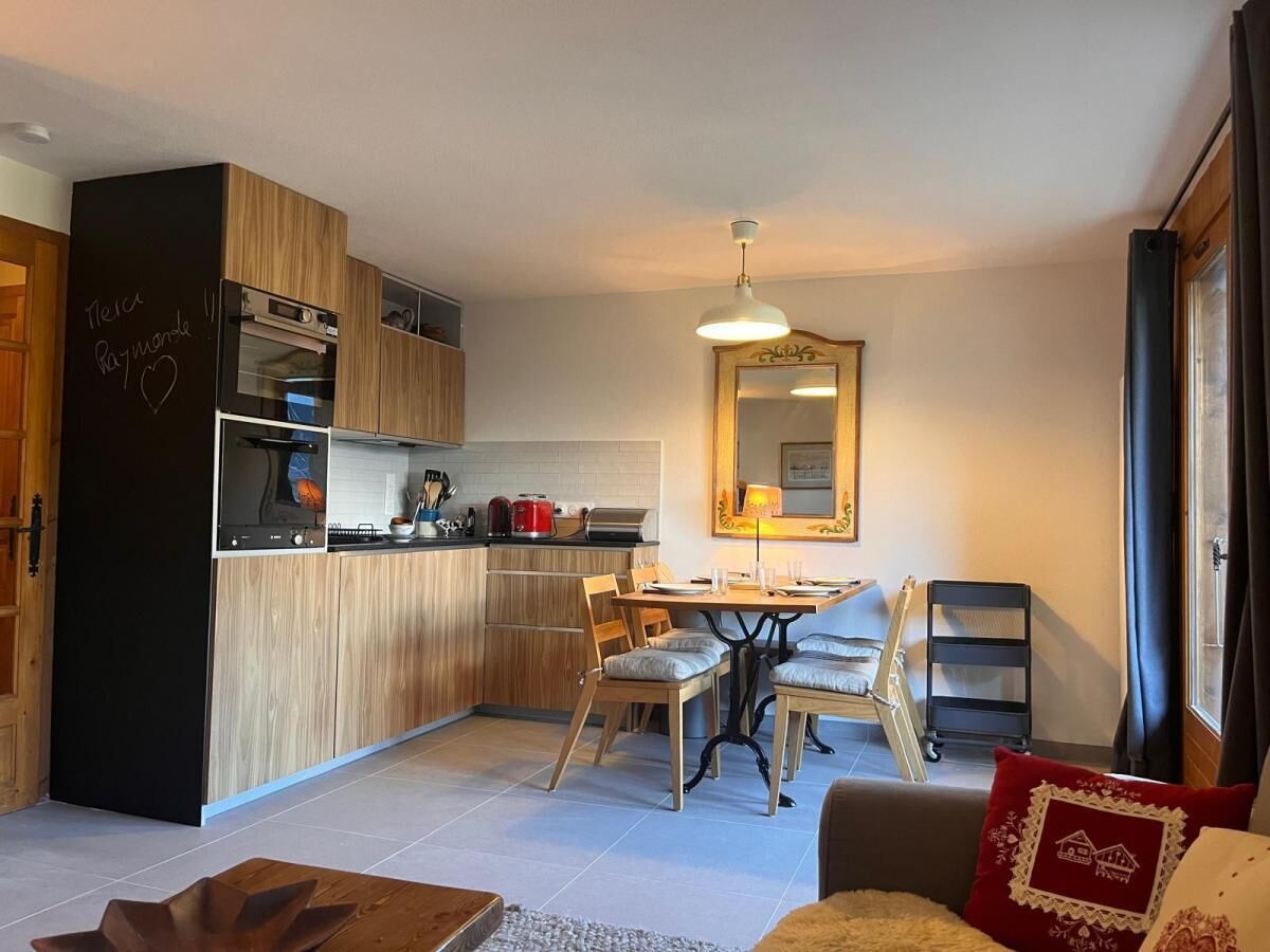 Une cuisine moderne avec des meubles en bois, un coin repas avec une table et des chaises, et un salon avec un canapé et un coussin rouge.