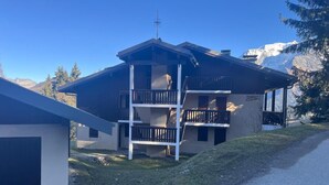 Un chalet de dos pisos con un balcón, un telesilla y montañas al fondo.