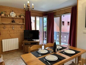 Uma área de jantar de madeira com mesa posta para quatro pessoas, televisão e vista para um deck de madeira.