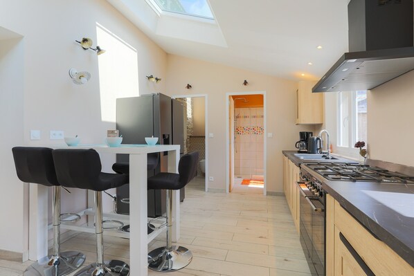 A modern kitchen with a skylight, a dining area with bar stools, and a view into the adjacent bathroom.
