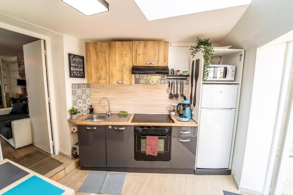 Een kleine keuken met donkere kastjes, een houten spatwand, een inbouwoven en een witte koelkast.