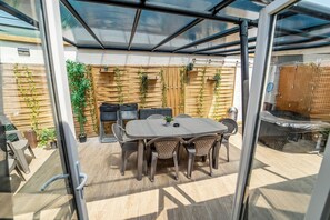 Un patio al aire libre con cerramiento de vidrio, una mesa redonda con sillas y una valla de madera con plantas trepadoras.