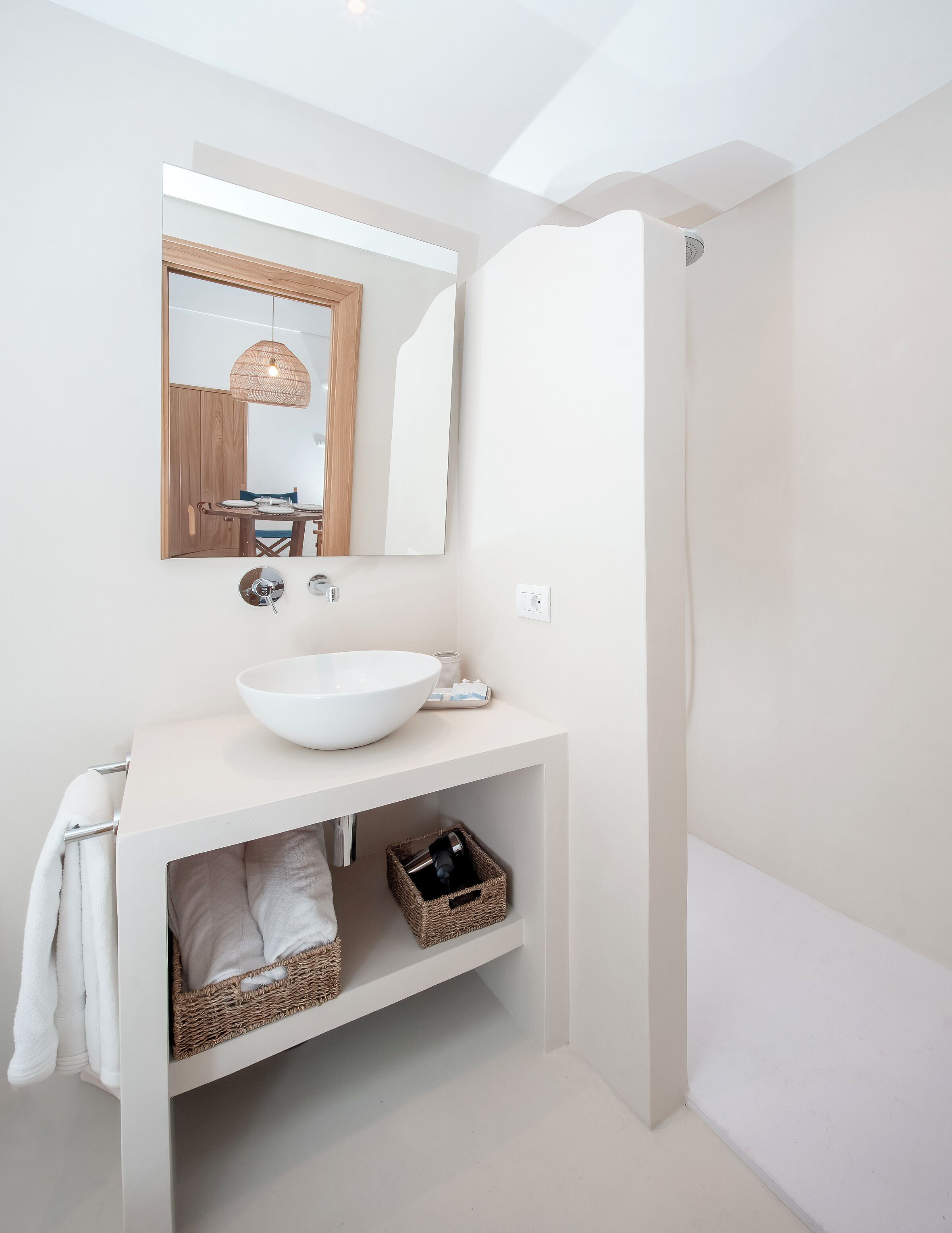 A modern bathroom with a white sink, mirror, and shower. There is a towel rack and a basket under the sink.