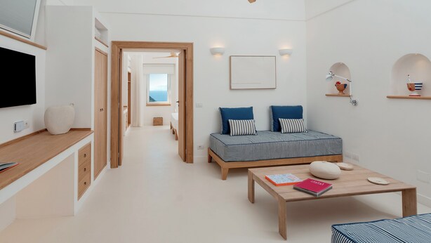 Et moderne, minimalistisk værelse med ventilator i træloft, seng med stribet sengetøj, sofabord i træ og et tv monteret på væggen.