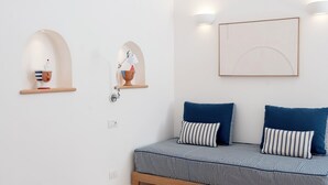 En minimalistisk stue med en stribet sofa, to vægmonterede hylder, et enkelt bord og et indrammet billede på væggen.