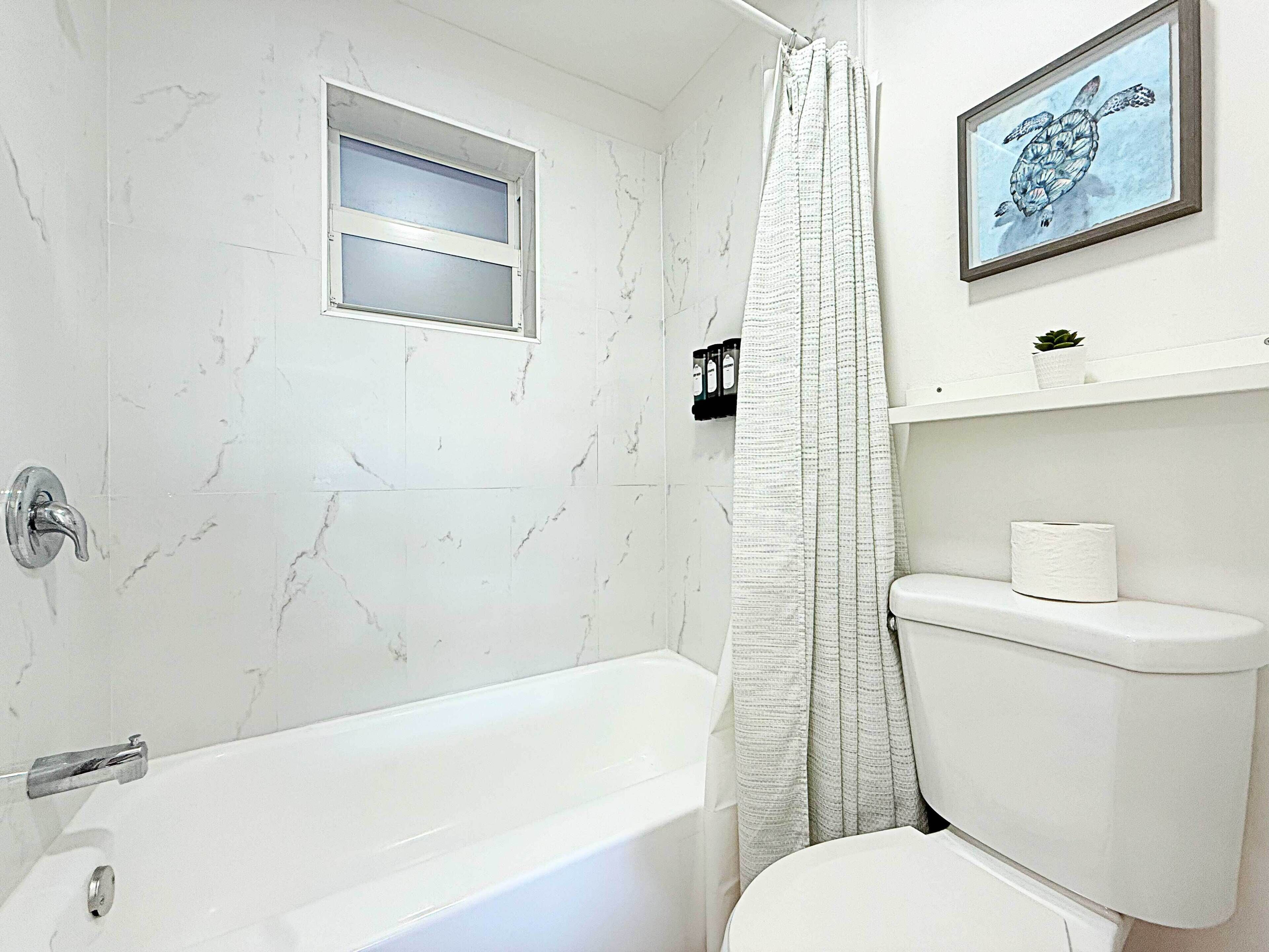 A bathroom with a bathtub, a toilet, a shower curtain, and a framed picture on the wall.