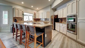A modern kitchen with white cabinetry, a central island with bar stools, stainless steel appliances, and a large window providing natural light. - North Scottsdale Gem w/ Pool , Hot Tub, Putting Green! (Scottsdale)