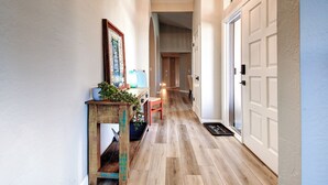 A hallway with wooden flooring, a wooden bench, a potted plant, a framed picture, and a door with a doormat. - North Scottsdale Gem w/ Pool , Hot Tub, Putting Green! (Scottsdale)