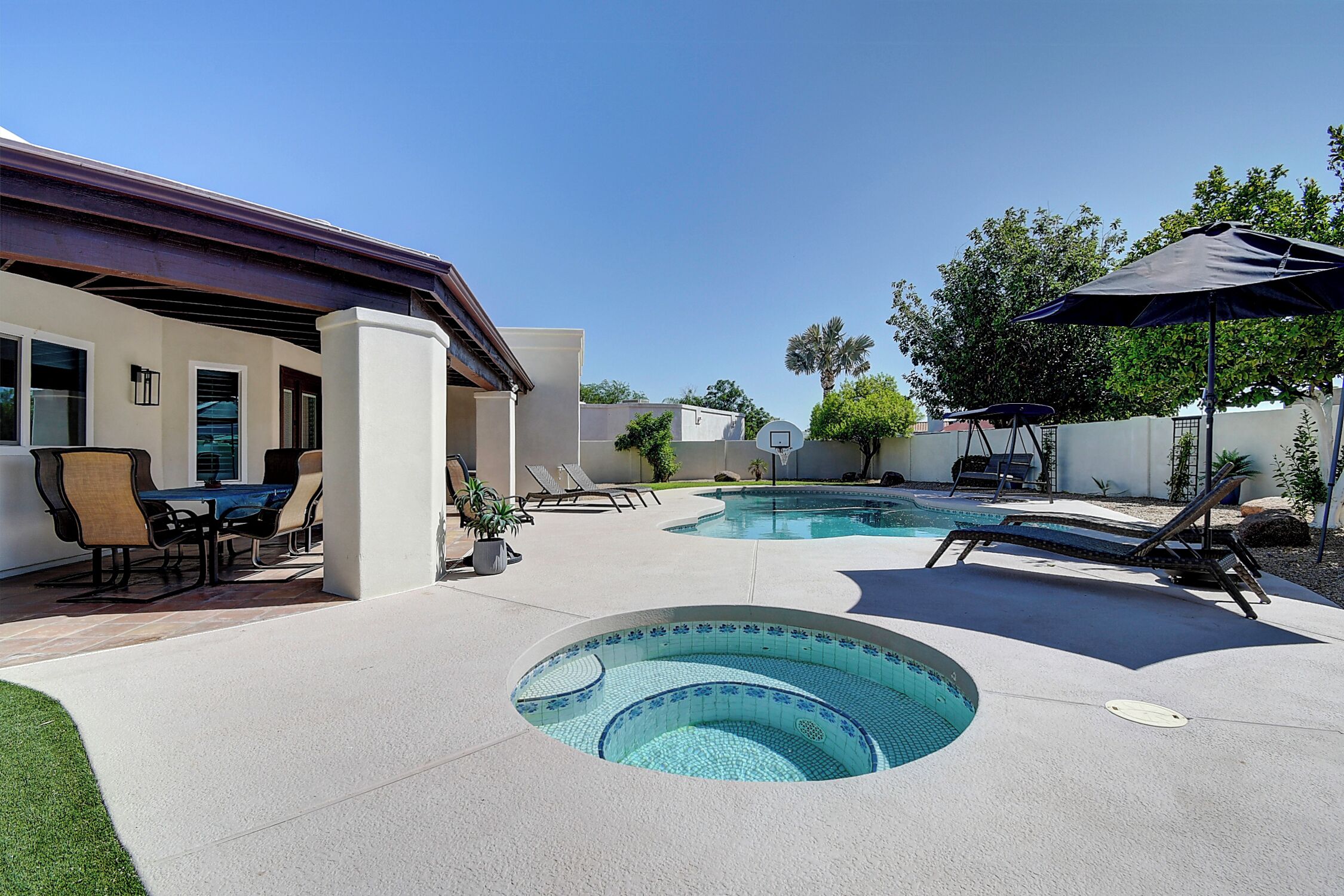 Un jardin avec une piscine, des chaises longues et un coin repas aménagé avec du mobilier d’extérieur.