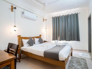 A neatly arranged bedroom with a wooden bed, bedside tables, a desk, and a window with curtains. - MTJ Hotels (Agra)