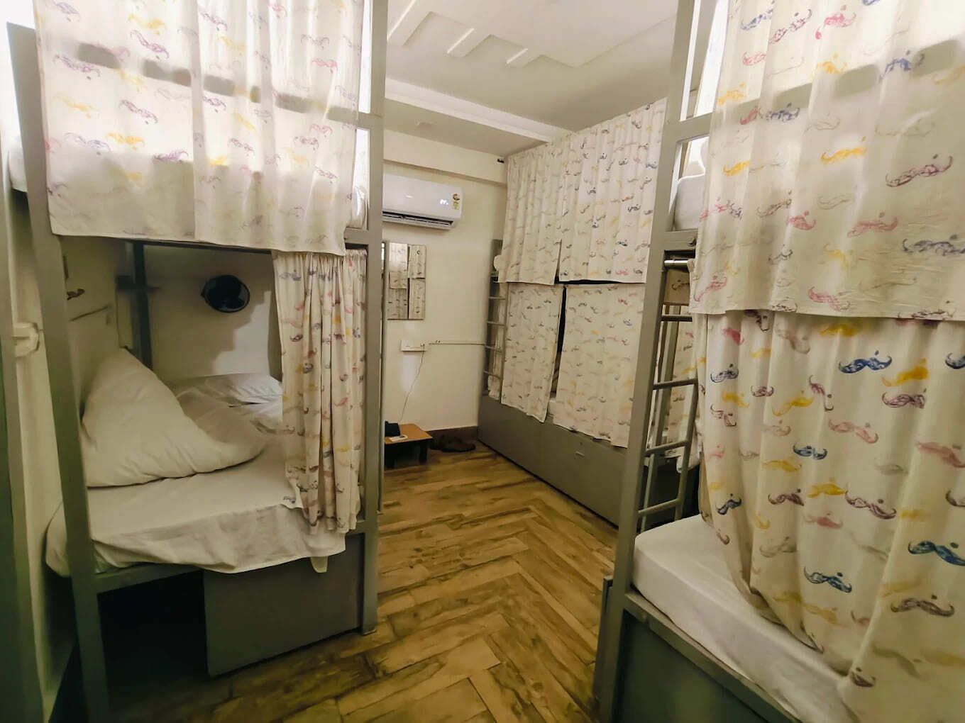 Un dormitorio con literas, suelo de madera y un equipo de aire acondicionado en la pared.
