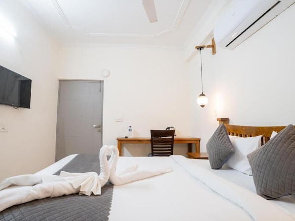 Et hotelværelse med seng, skrivebord, stol og fjernsyn på væggen.