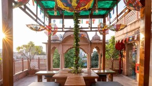 Un espace extérieur aménagé avec des tables et des bancs en bois, une structure décorative au-dessus et une vue sur la verdure en arrière-plan.