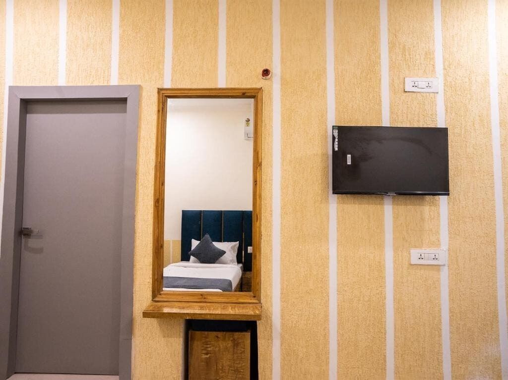 Une chambre d’hôtel avec un miroir à cadre en bois, un lit avec une tête de lit bleue et un téléviseur à écran plat fixé au mur.