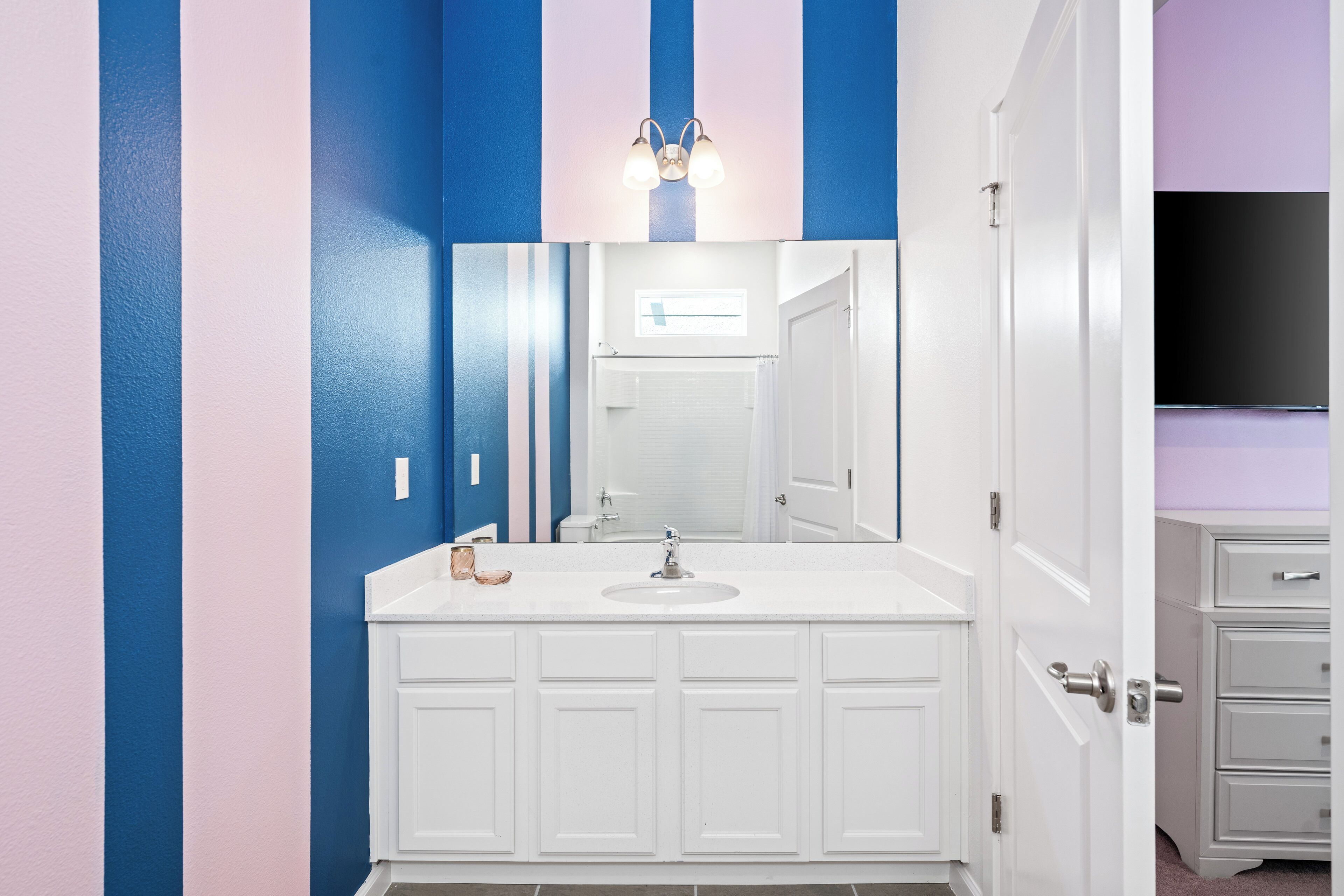 A bathroom with a white vanity, a mirror, and a blue and pink striped wall.