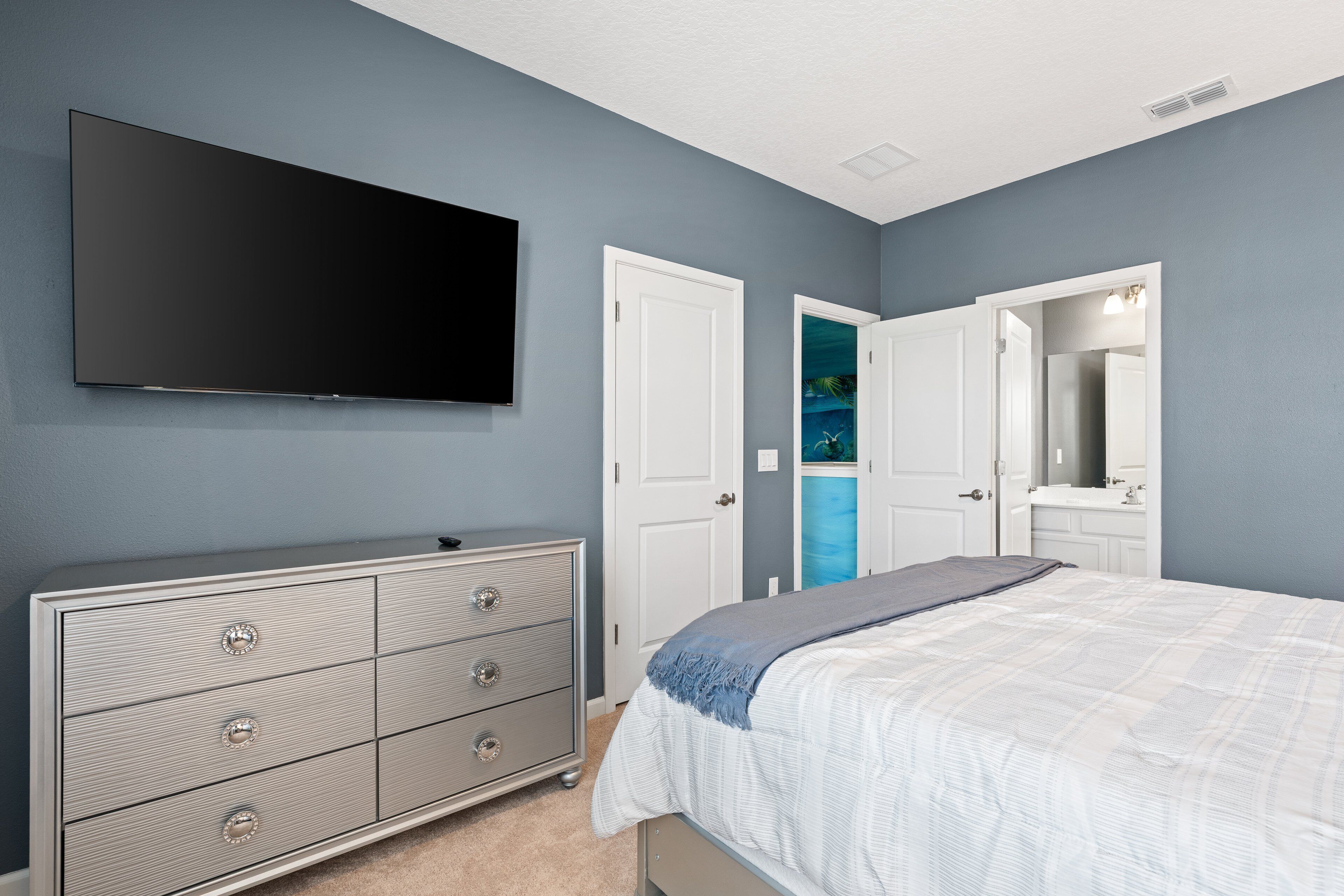 A bedroom with a bed, dresser, and a TV mounted on the wall.
