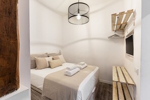 A bedroom with a bed, a hanging light fixture, a wooden bench, and a window with blinds.
