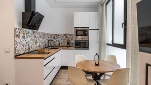 A modern kitchen with a wooden countertop, white cabinets, and a built-in oven. There is a dining area with a round table and four chairs. - Waou Chamberi VIII - Short Term Rental (Madrid)