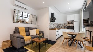 A modern apartment with a grey sofa, a dining table, and a kitchen area with white cabinets and stainless steel appliances. - Waou Chamberi VIII - Short Term Rental (Madrid)