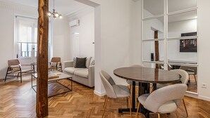 Una sala de estar moderna con piso de madera en patrón de espiga, una mesa redonda de comedor con sillas, un sofá y un espejo grande en la pared.
