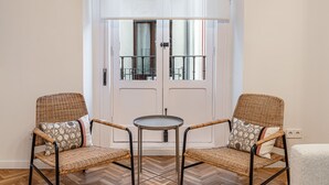 Una habitación con dos sillas de mimbre, una mesita redonda y una puerta blanca con un portón de metal.