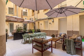 Une vaste terrasse extérieure dotée de nombreuses tables et chaises, ombragée par de grands parasols et entourée de plantes en pot.