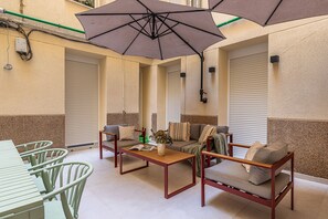 Un espace extérieur ensoleillé, aménagé avec une table et des chaises, un canapé et un grand parasol pour créer de l’ombre.