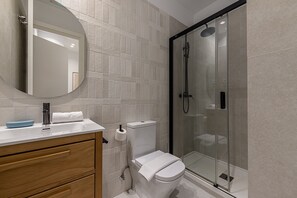 Une salle de bain moderne avec une douche à parois de verre, des toilettes blanches et un meuble-lavabo en bois avec un miroir.