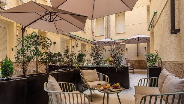 Een gezellig buitenverblijf met comfortabele stoelen en tafels, omgeven door potplanten en parasols voor de schaduw.