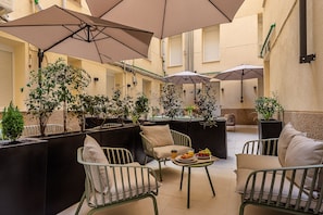 Een gezellig buitenverblijf met comfortabele stoelen en tafels, omgeven door potplanten en parasols voor de schaduw.