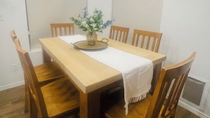 A dining room with a wooden table, four chairs, a chandelier, and a vase with flowers.