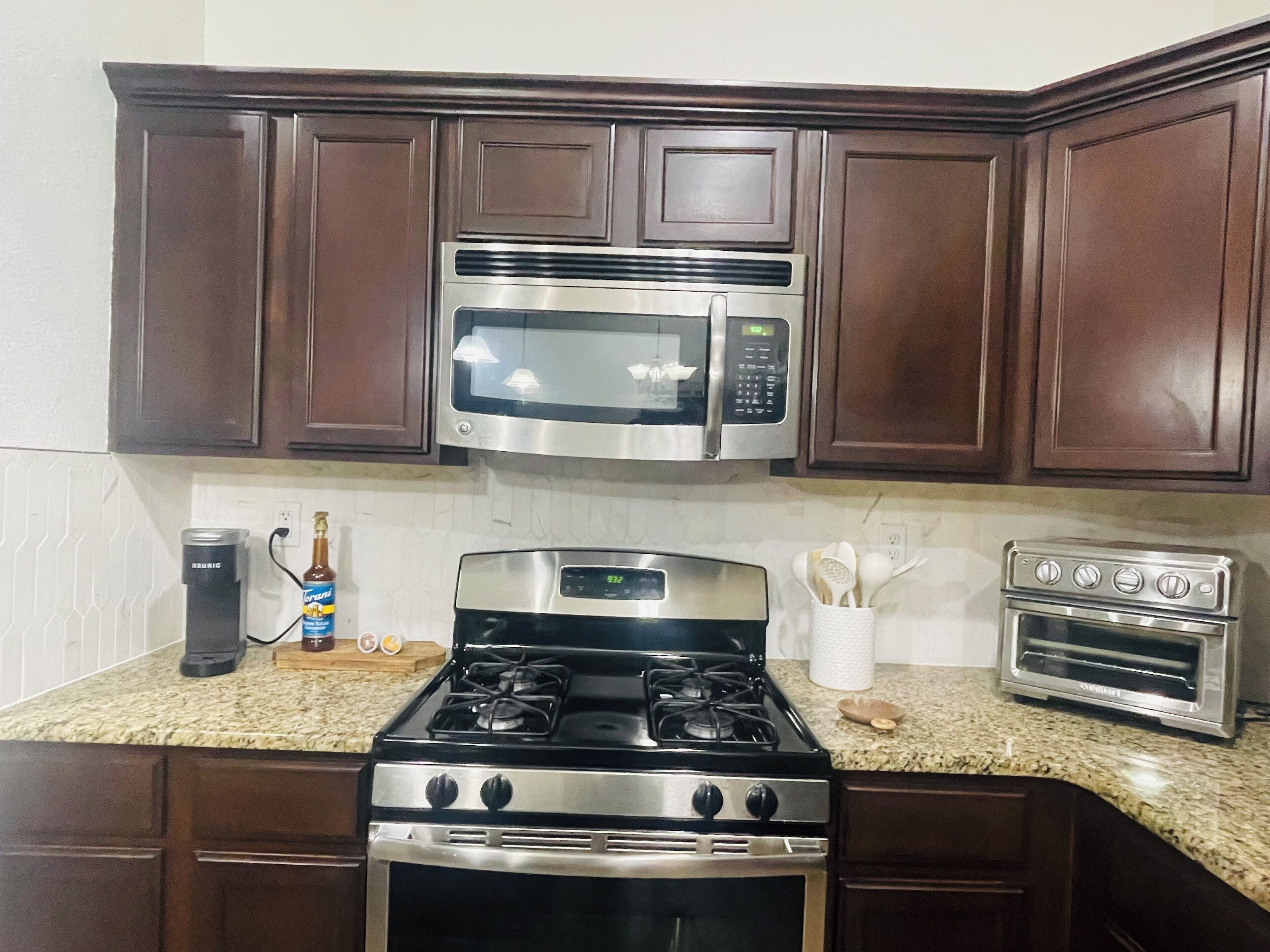A kitchen with dark wooden cabinets, a stainless steel microwave, a gas stove, and a toaster oven.