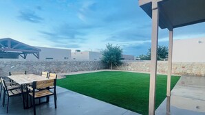A patio with a table and chairs, a stone wall, and a green lawn.