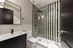 Un baño moderno con un lavamanos blanco, un inodoro y una zona de ducha con paredes de vidrio a rayas.