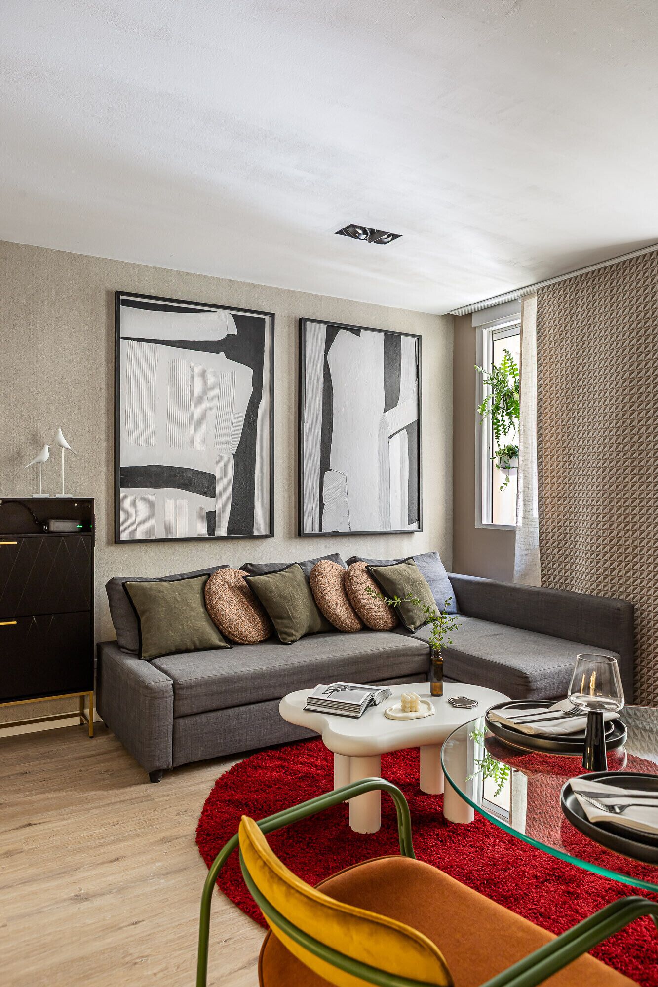 A modern living room with a grey sofa, abstract wall art, a red rug, and a glass coffee table.