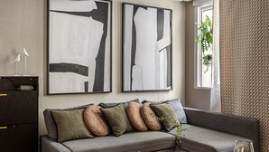 A modern living room with a grey sofa, abstract wall art, a red rug, and a glass coffee table. - Waou La Latina V - Short Term Rental (Madrid)