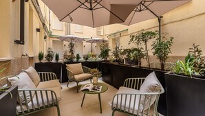 A cozy outdoor seating area with cushioned chairs and tables, surrounded by potted plants and umbrellas providing shade. - Waou Urban Home Chamberi I (Madrid)