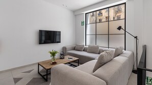 A modern living room with a large window, a flat-screen TV, a sofa, a coffee table, and a floor lamp. - Waou Urban Home Chamberi I (Madrid)