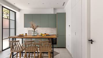 A modern kitchen with a wooden table and chairs, a vase with dried flowers, and a breakfast setting.