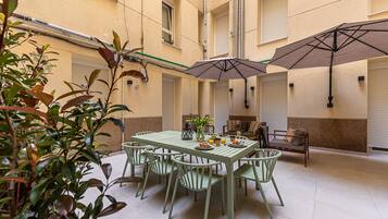 A patio with a table and chairs, a small sofa, and umbrellas.