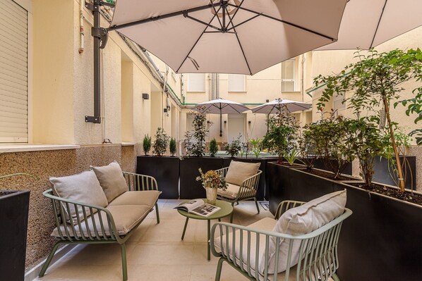 A cozy outdoor seating area with metal chairs and a table, surrounded by potted plants and umbrellas.