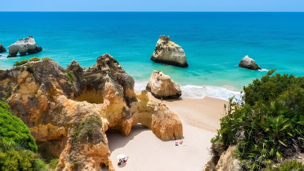 Ein Strand mit großen Felsformationen, klarem türkisblauem Wasser und einem Sandstrand.